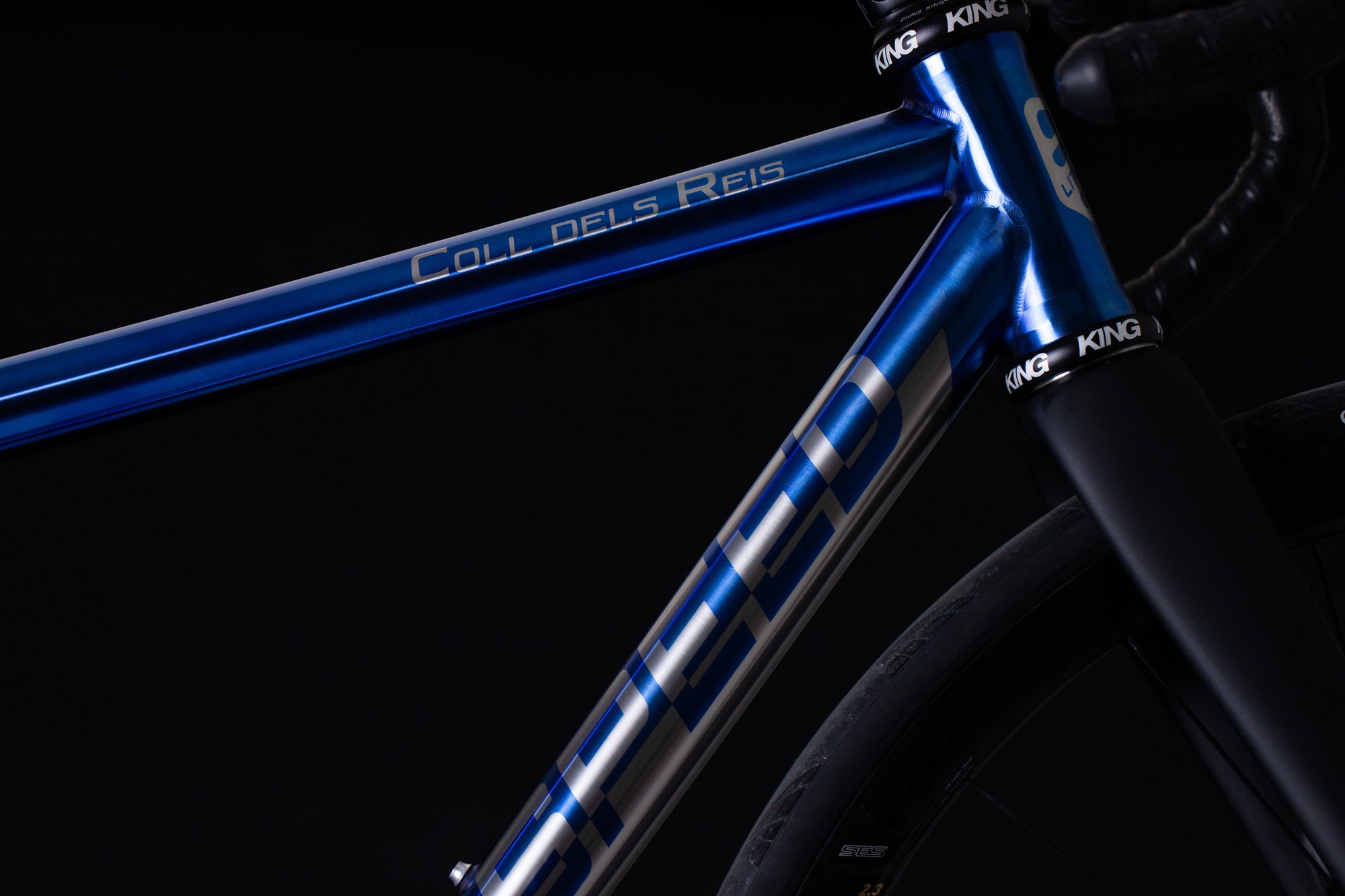 Close-up of a blue bicycle frame with 'Coll dels Reis' branding on a black background