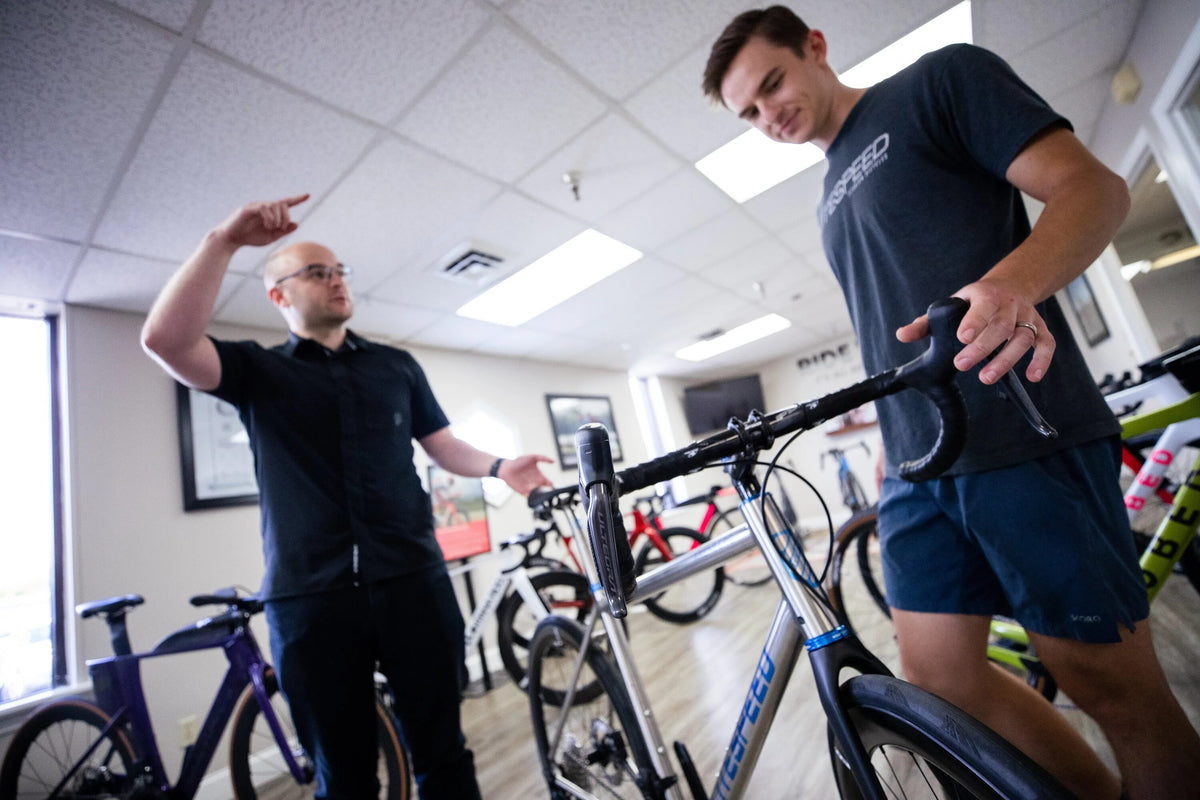 Two men examining a bicycle in an indoor setting, likely a bike shop.