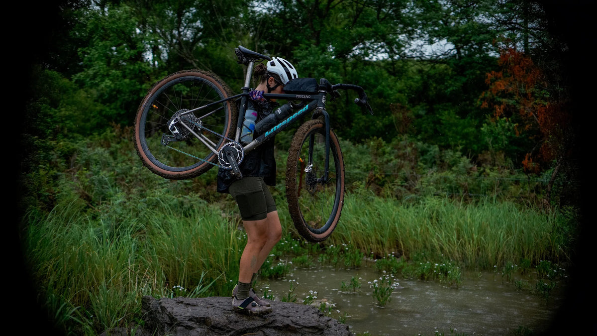 Person carrying a mountain bike through a forest